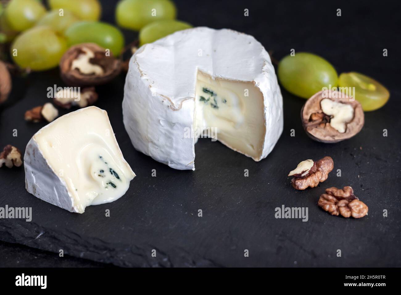 Tipo di formaggio Brie. Formaggio morbido con uva e noci su sfondo nero Foto Stock