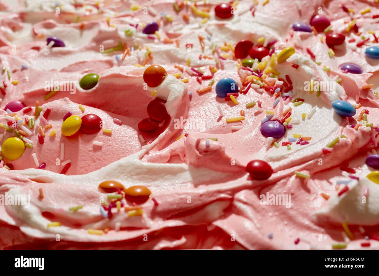 Gelato alla fragola e alla vaniglia con caramelle al cioccolato ricoperte di zucchero e spolverini colorati per una festa per bambini da vicino Foto Stock