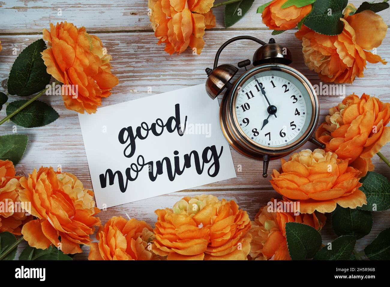 Buona carta del mattino e sveglia con decorazione di fiori d'arancio su sfondo di legno Foto Stock