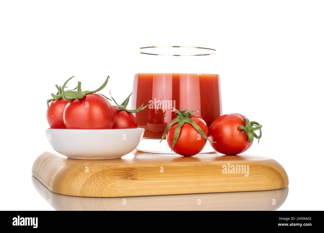 Una tazza di vetro con succo di pomodoro e diversi pomodori su un vassoio di bambù, primo piano, isolato su bianco. Foto Stock