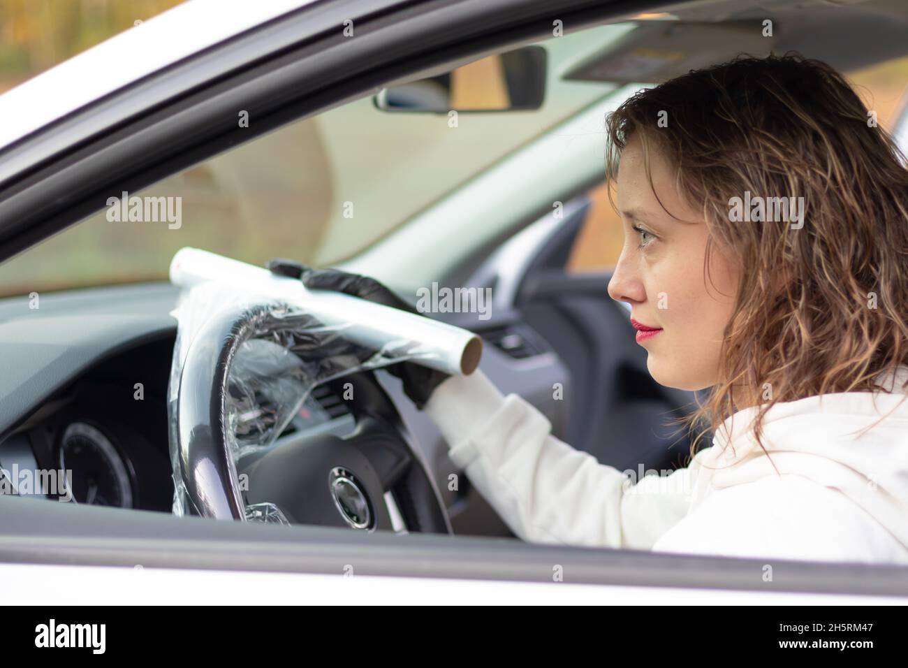 Una bella giovane donna conducente in una giacca bianca e guanti neri  avvolge il volante di