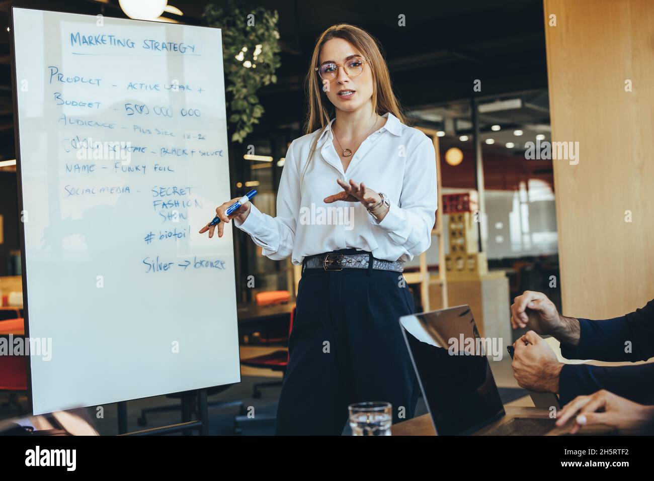 Donna d'affari intelligente che discute le sue idee di marketing con il suo team in un ambiente di lavoro moderno. Giovane donna d'affari fiduciosa che dà una presentazione durante un m Foto Stock