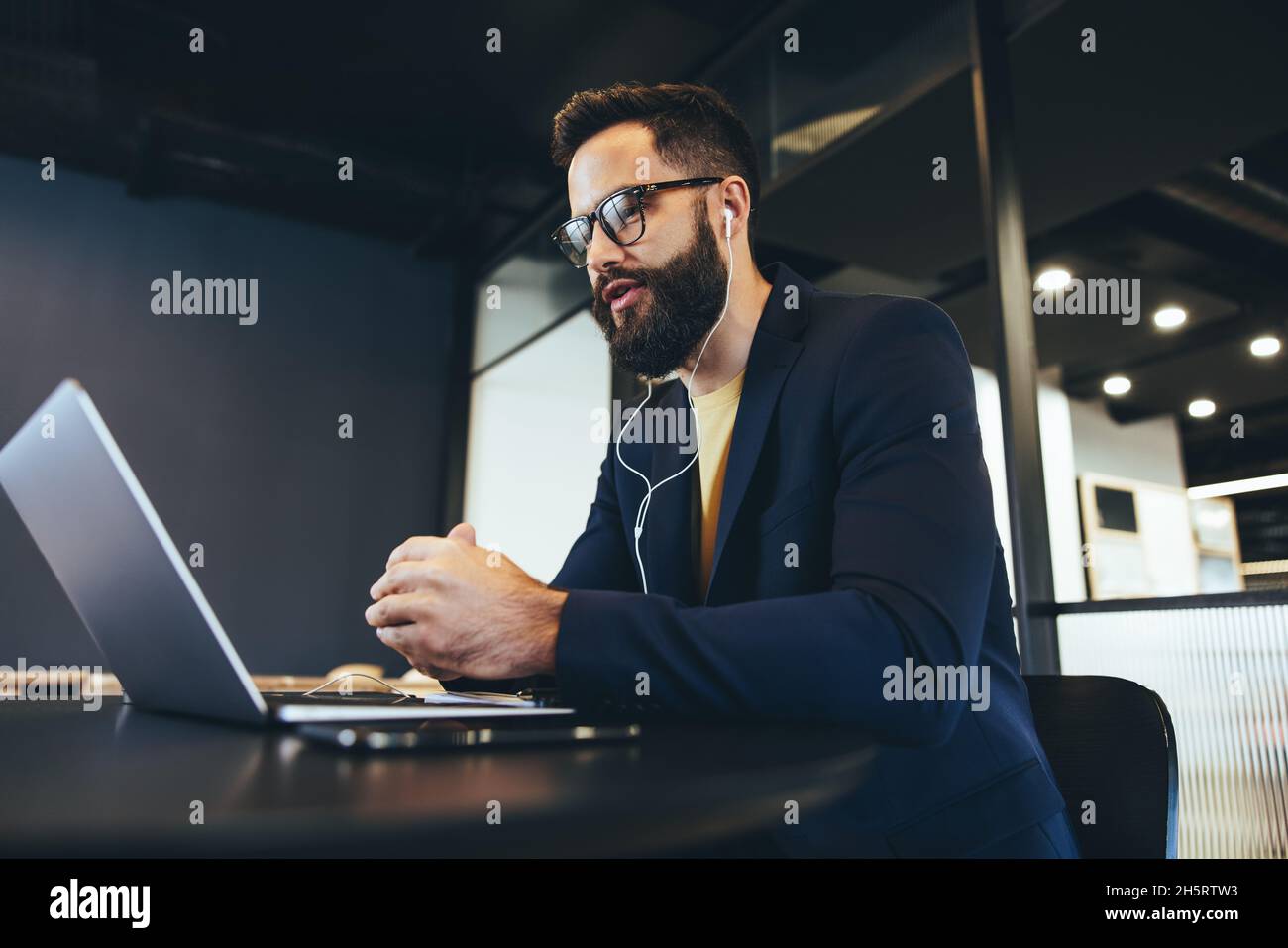 Imprenditore maschile che partecipa a una riunione virtuale in un ufficio. Giovane uomo d'affari che indossa le cuffie durante una videochiamata in ufficio. uomini d'affari Foto Stock