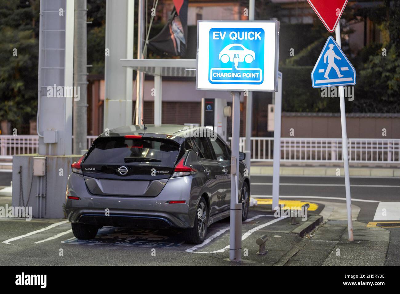 Nissan Leaf viene caricato presso il punto di ricarica rapida EV per i veicoli elettrici. Segnale di accensione della luce blu Foto Stock