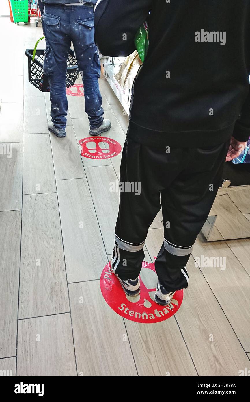 Le persone sul mercato sono in linea osservando la distanza sociale secondo i segni indicati Foto Stock