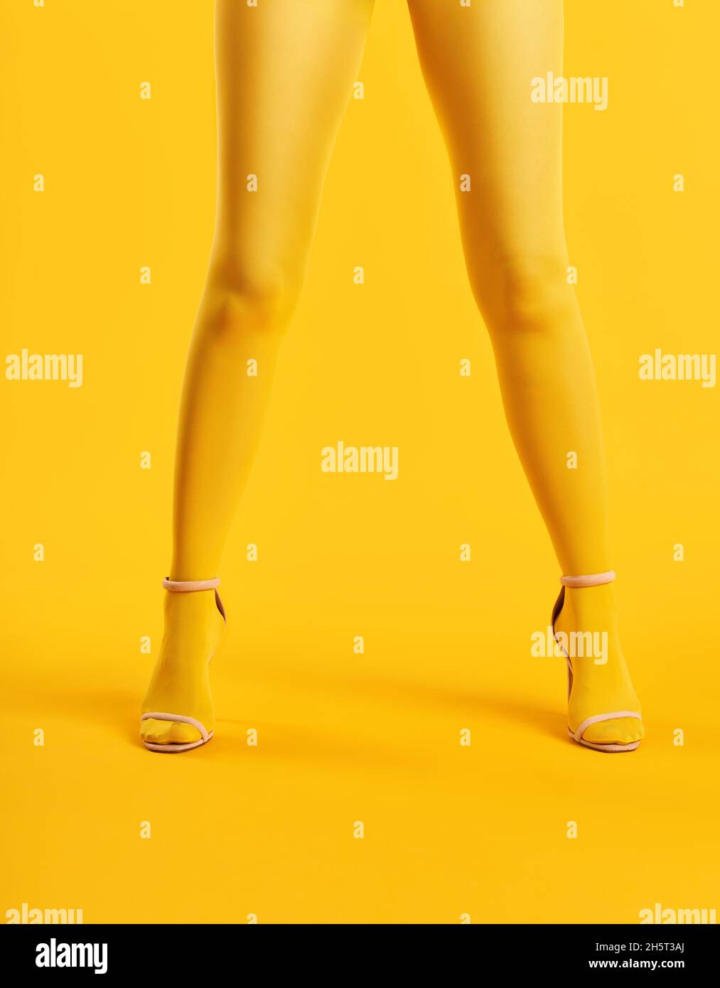 Lunghe e sottili gambe di giovane donna in collant gialli e scarpe eleganti con tacco alto su sfondo giallo. Concetto di arte pop Foto Stock
