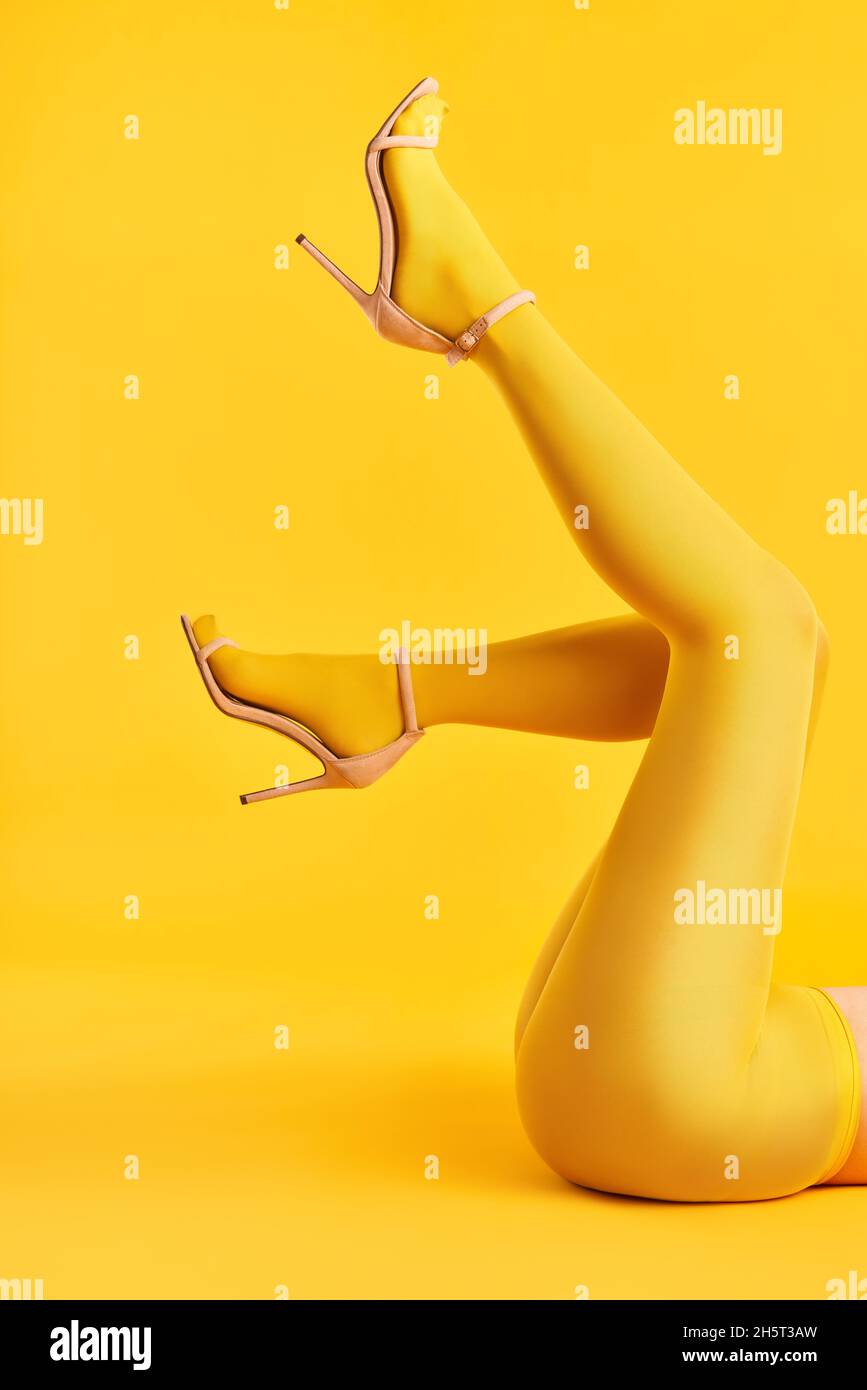 Lunghe e sottili gambe di giovane donna in collant gialli e scarpe eleganti con tacco alto su sfondo giallo. Pop art, bellezza femminile, concetto di femminilità Foto Stock