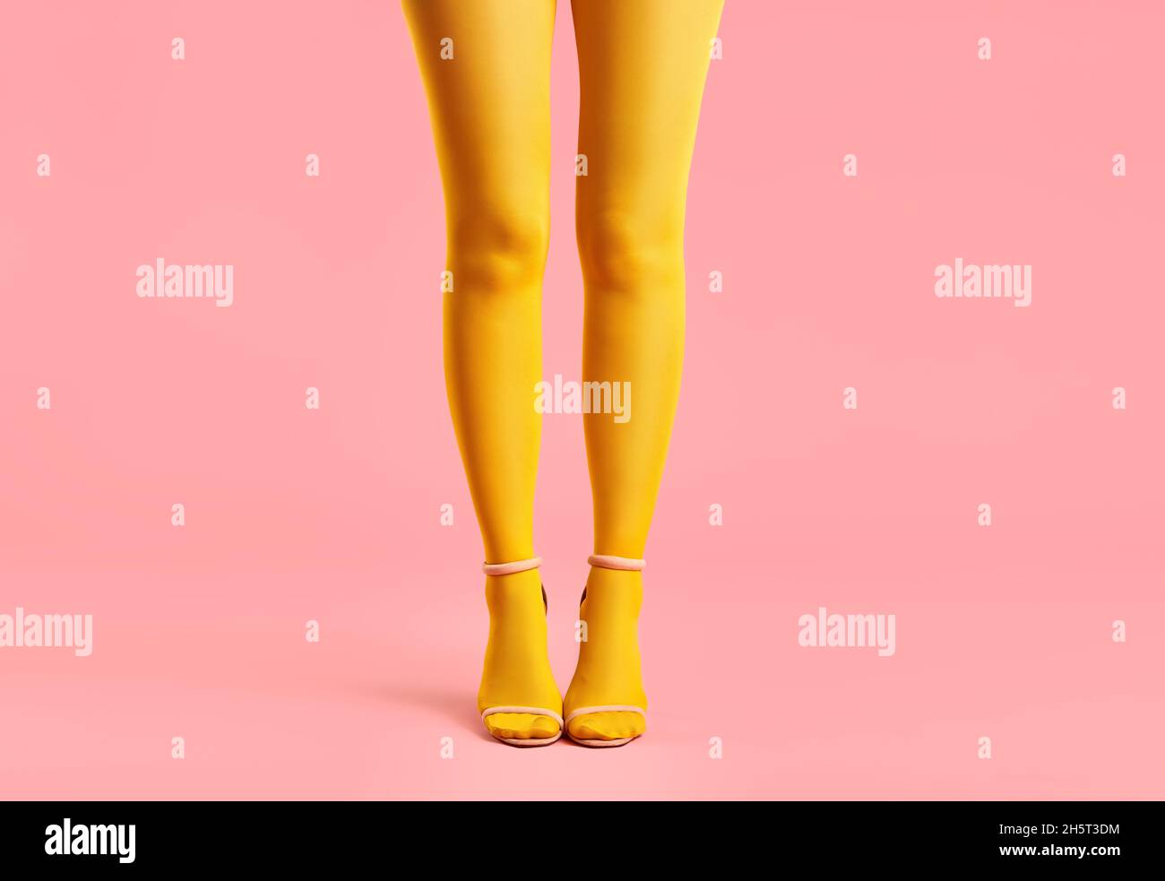 Lunghe e sottili gambe di giovane donna in collant gialli e scarpe eleganti con tacco alto su sfondo rosa. Concetto di arte pop Foto Stock