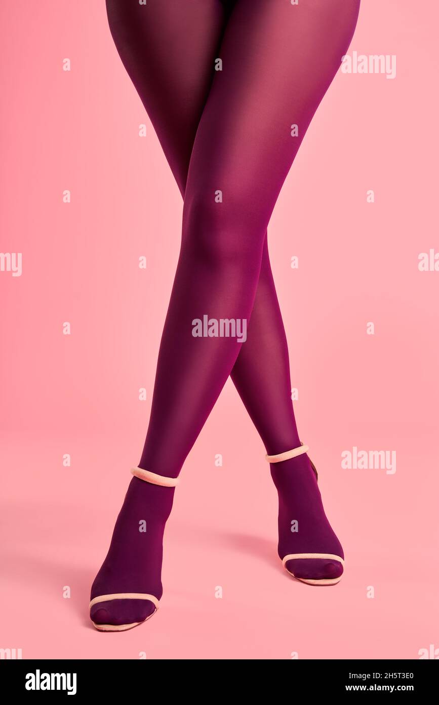 Lunghe e sottili gambe incrociate di giovane donna in collant rosa su sfondo rosa. Pop art, concetto femminile Foto Stock