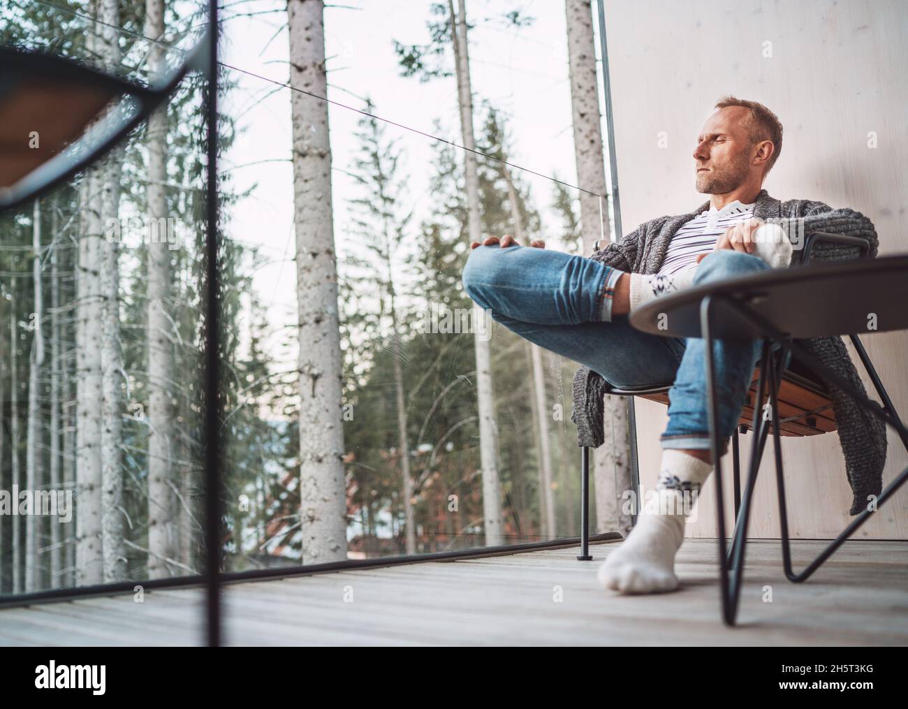 Ritratto di uomo di mezza età vestito cardigan aperto, jeans, e calze calde  seduti sul balcone