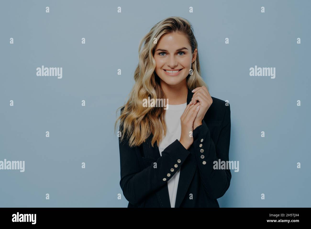 Simpatico studente femminile positivo in elegante abito casual in posa contro la parete blu studio Foto Stock