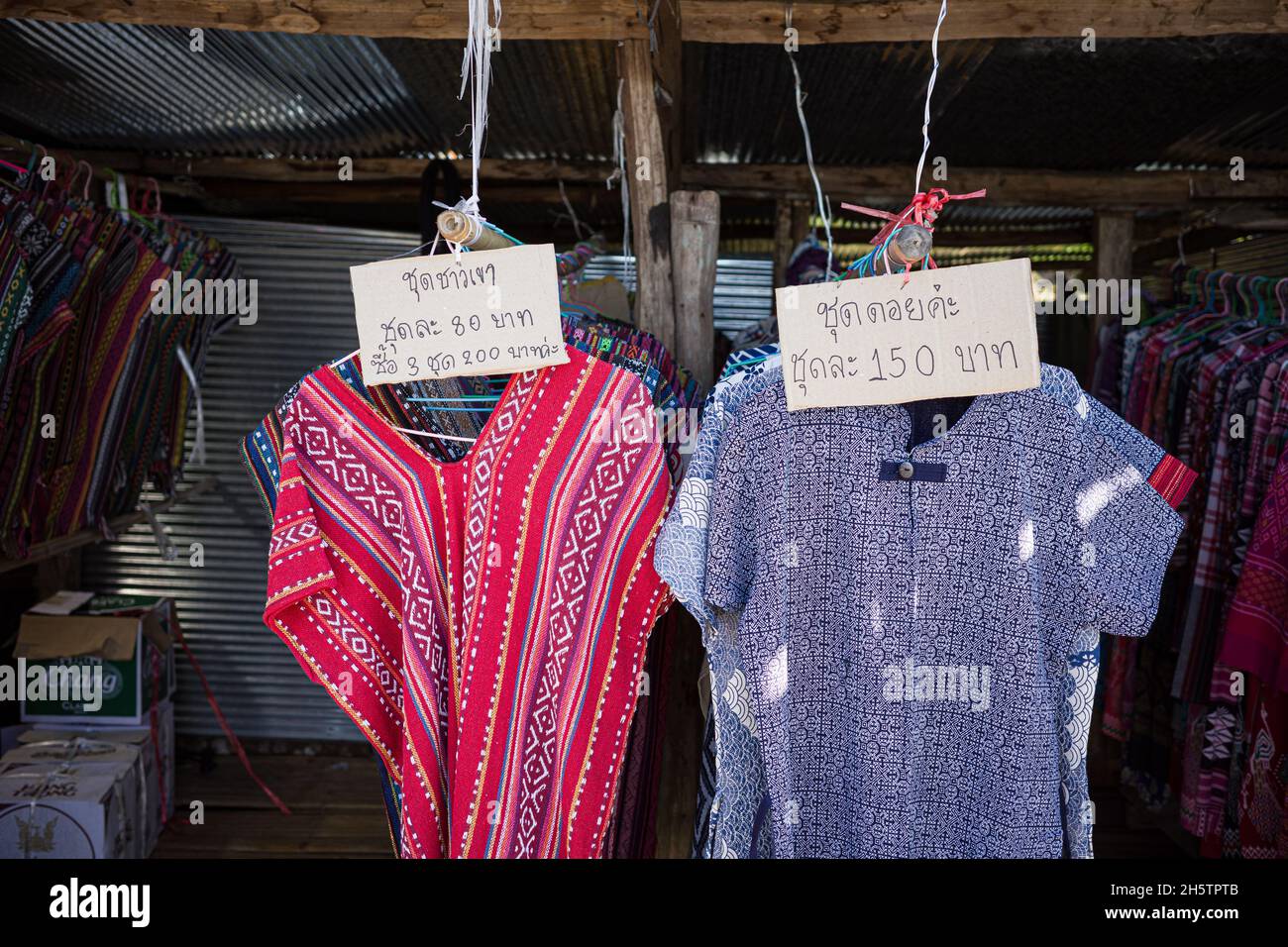 Colorate magliette alpinistiche in blu e rosso appese su scaffale con etichetta prezzo in lingua thailandese del negozio di abbigliamento rurale. Foto Stock