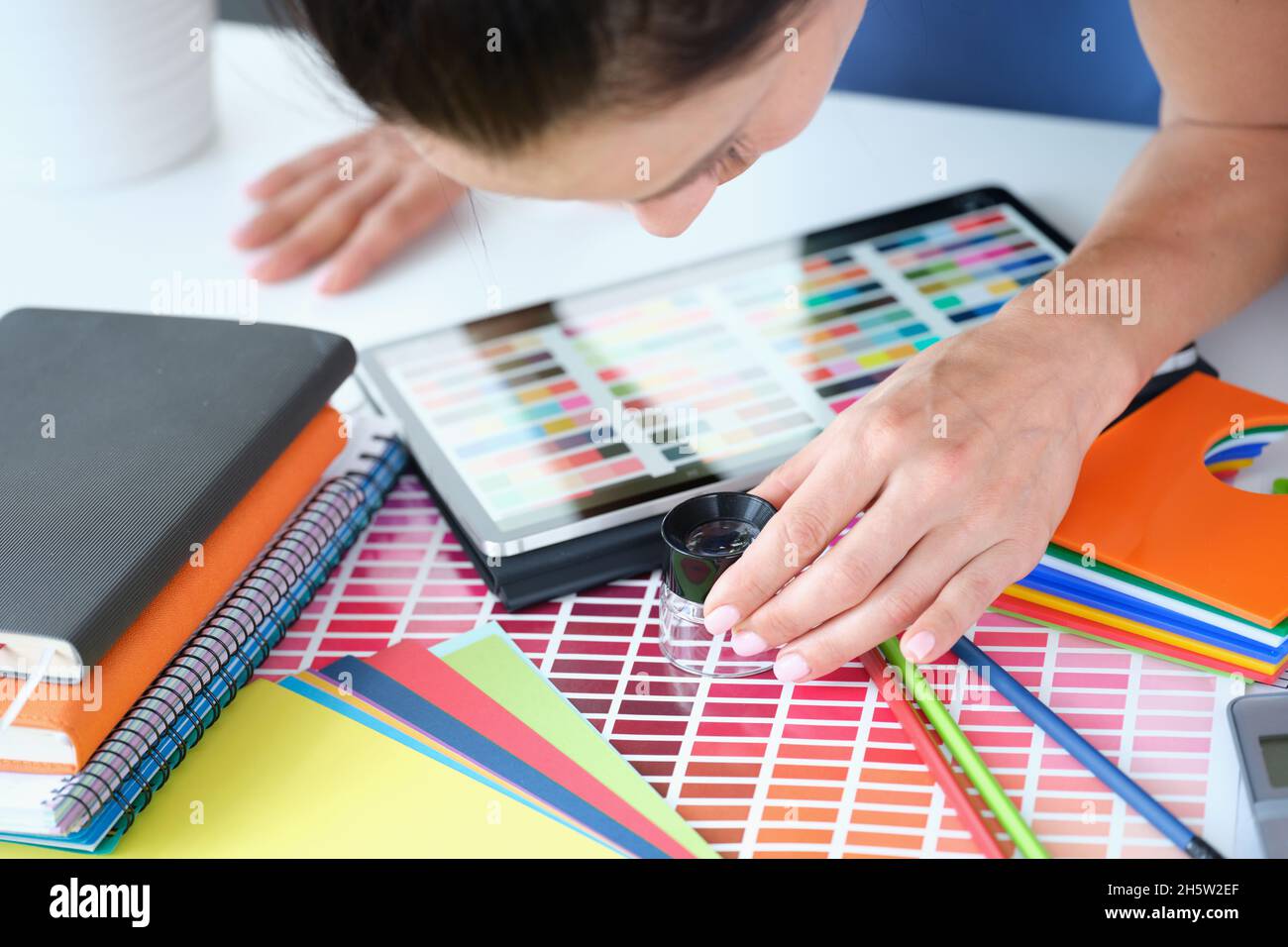 Donna designer guarda attraverso lente d'ingrandimento alla tavolozza di colori con diverse sfumature di colori Foto Stock