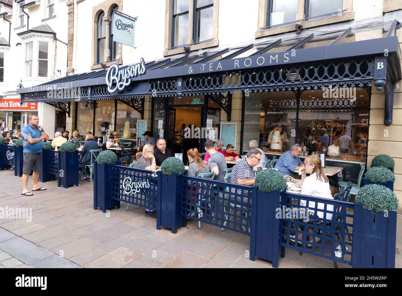 Tea Rooms UK; persone che si siedono all'esterno bere tè in estate, Brysons Tea Rooms and Cafe, Keswick Town Center, Keswick Cumbria UK Foto Stock