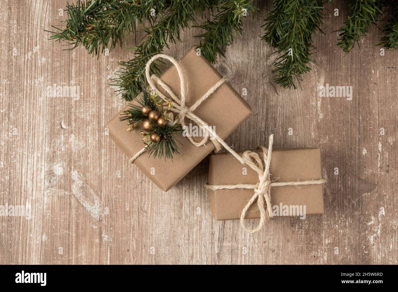 dettaglio delle confezioni regalo avvolte in carta con un arco a corda e un piccolo ornamento, sfondo con tessitura in legno e ramo d'albero, dettaglio della texture Foto Stock
