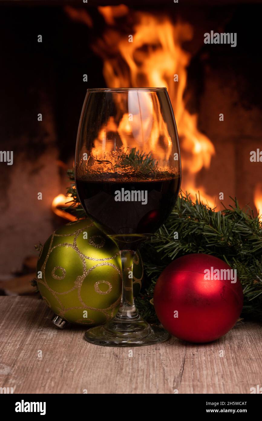 bicchiere con vino rosso decorato con combilli di natale, sullo sfondo un camino con fuoco, luogo accogliente, bevanda e celebrazione di un appuntamento Foto Stock