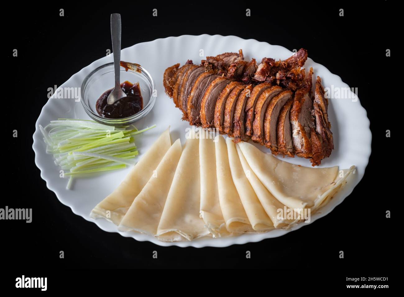 Anatra di Pechino, anatra croccante fritta cinese, servita con salsa di hoisin, pancake e cetriolo, in un piatto bianco su sfondo nero. Foto Stock