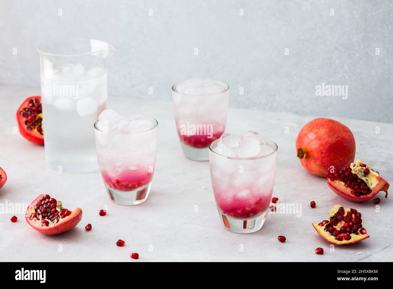 Rinfrescante melograno bere in bicchieri con semi di melograno e ghiaccio, brocca di acqua fredda con agrumi, melograni tagliati con semi Foto Stock