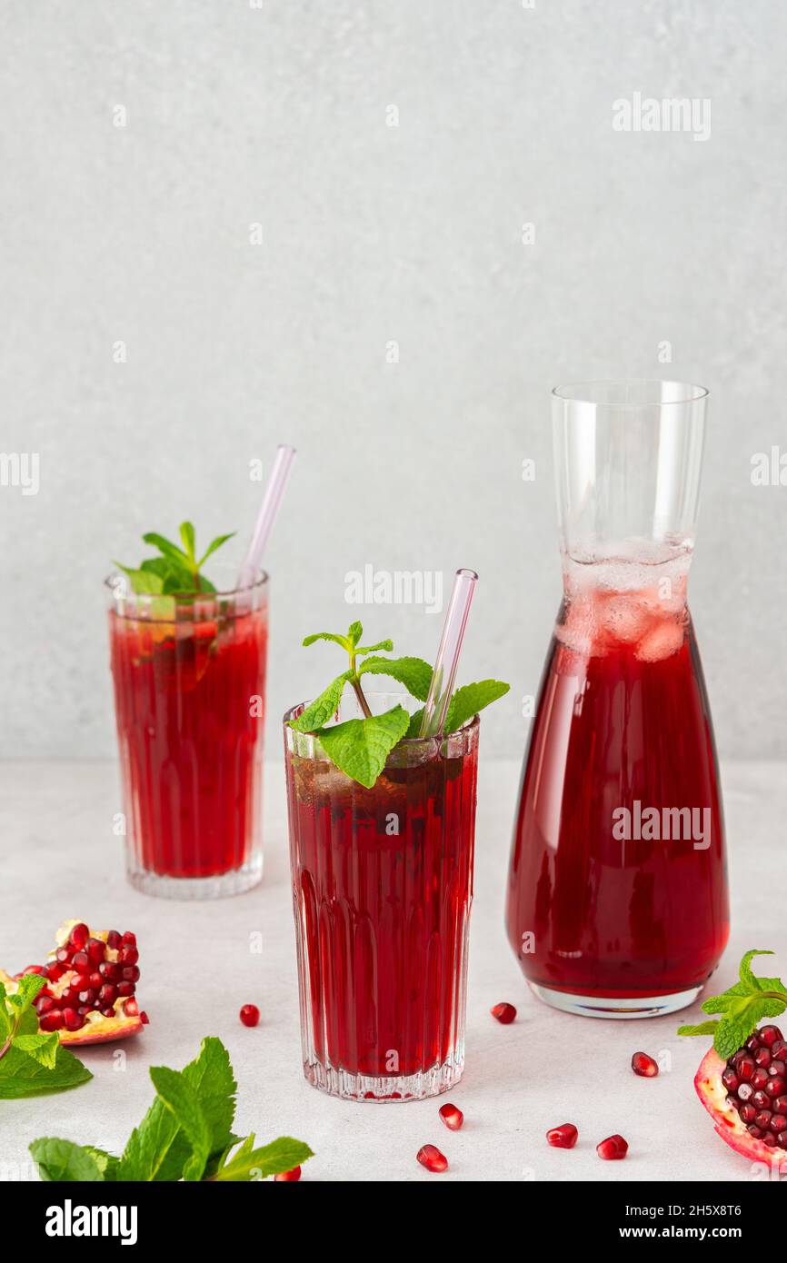 Rinfrescante succo di melograno in bicchieri con paglia di menta e vetro, caraffa di succo di frutta e ghiaccio, bevanda fredda Foto Stock