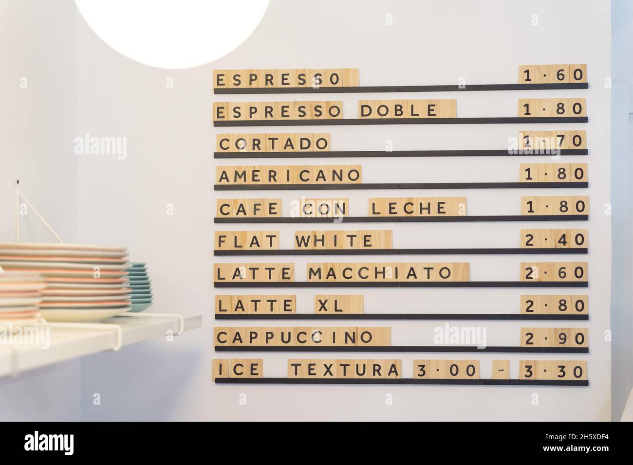 Menu a tavola con varie bevande a base di caffè e prezzi su parete bianca vicino al banco con stoviglie in moderna e leggera caffetteria con luce brillante Foto Stock