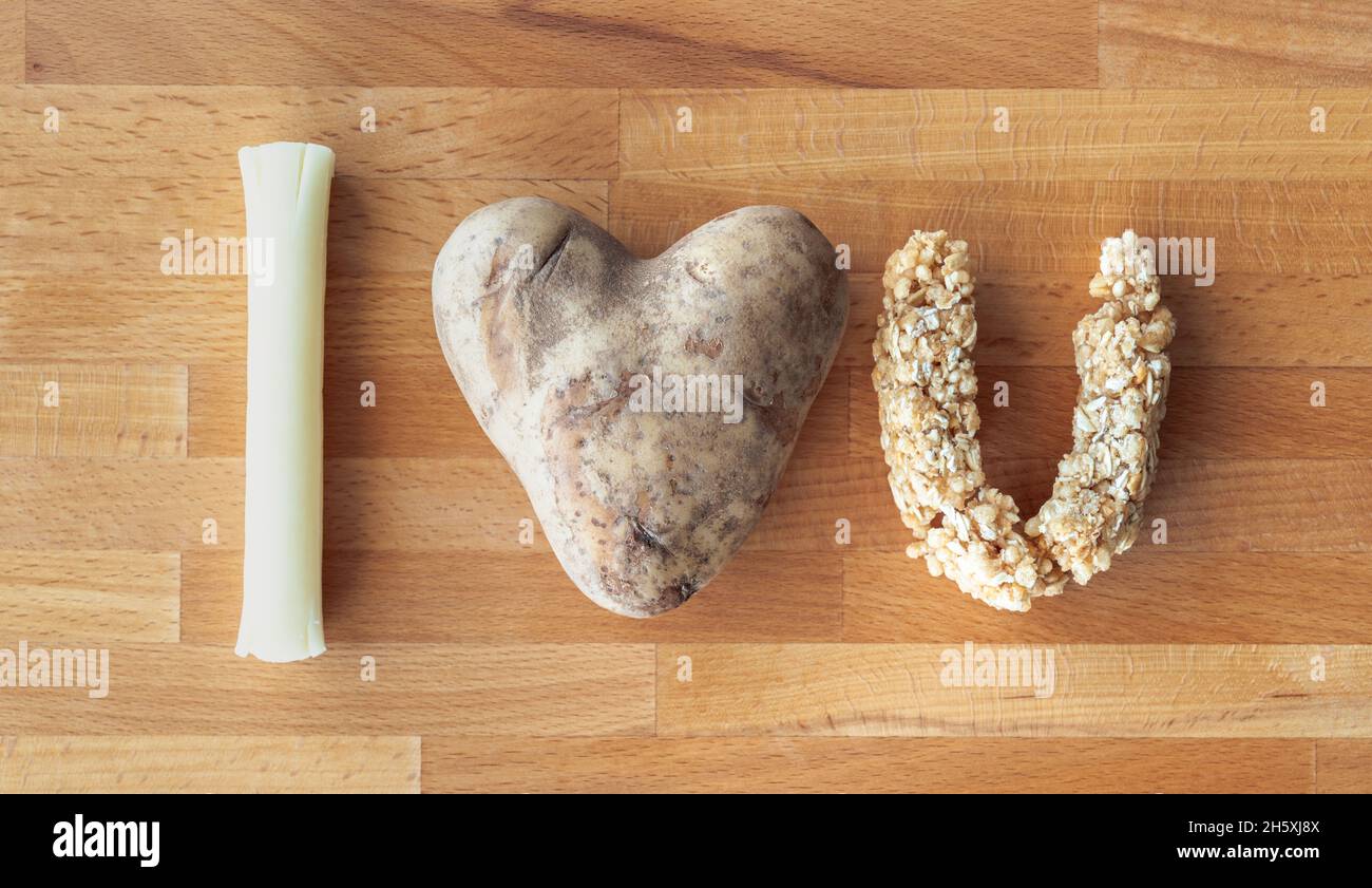 Un messaggio i love you scritto usando gli articoli del cibo compreso un bastone del formaggio della stringa della mozzarella, patate a forma di cuore e barra della granola nella forma di u Foto Stock