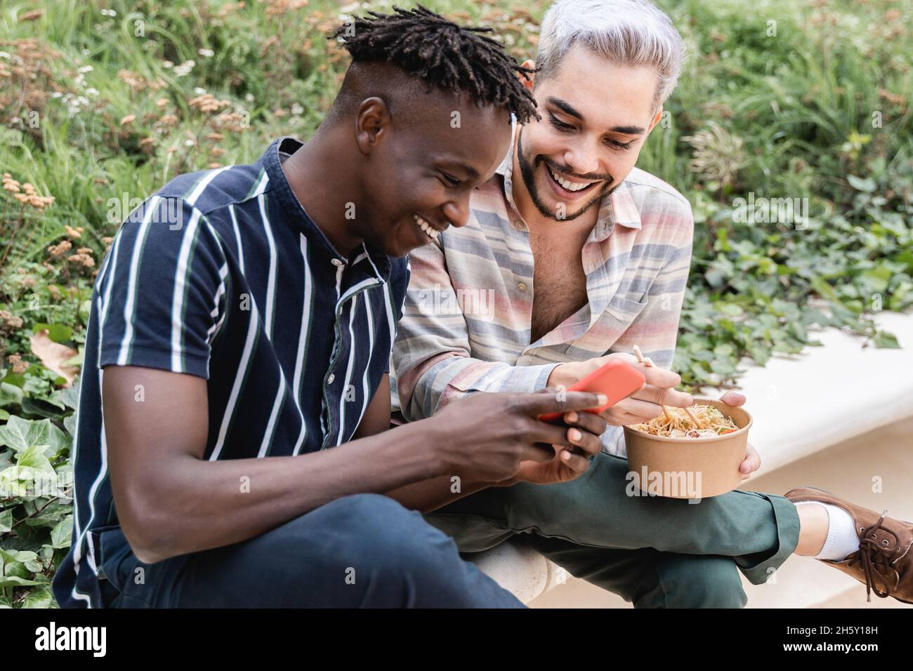 Amici felici e diversi che mangiano cibo take away all'aperto in città - Focus on nonbinany gay man Foto Stock