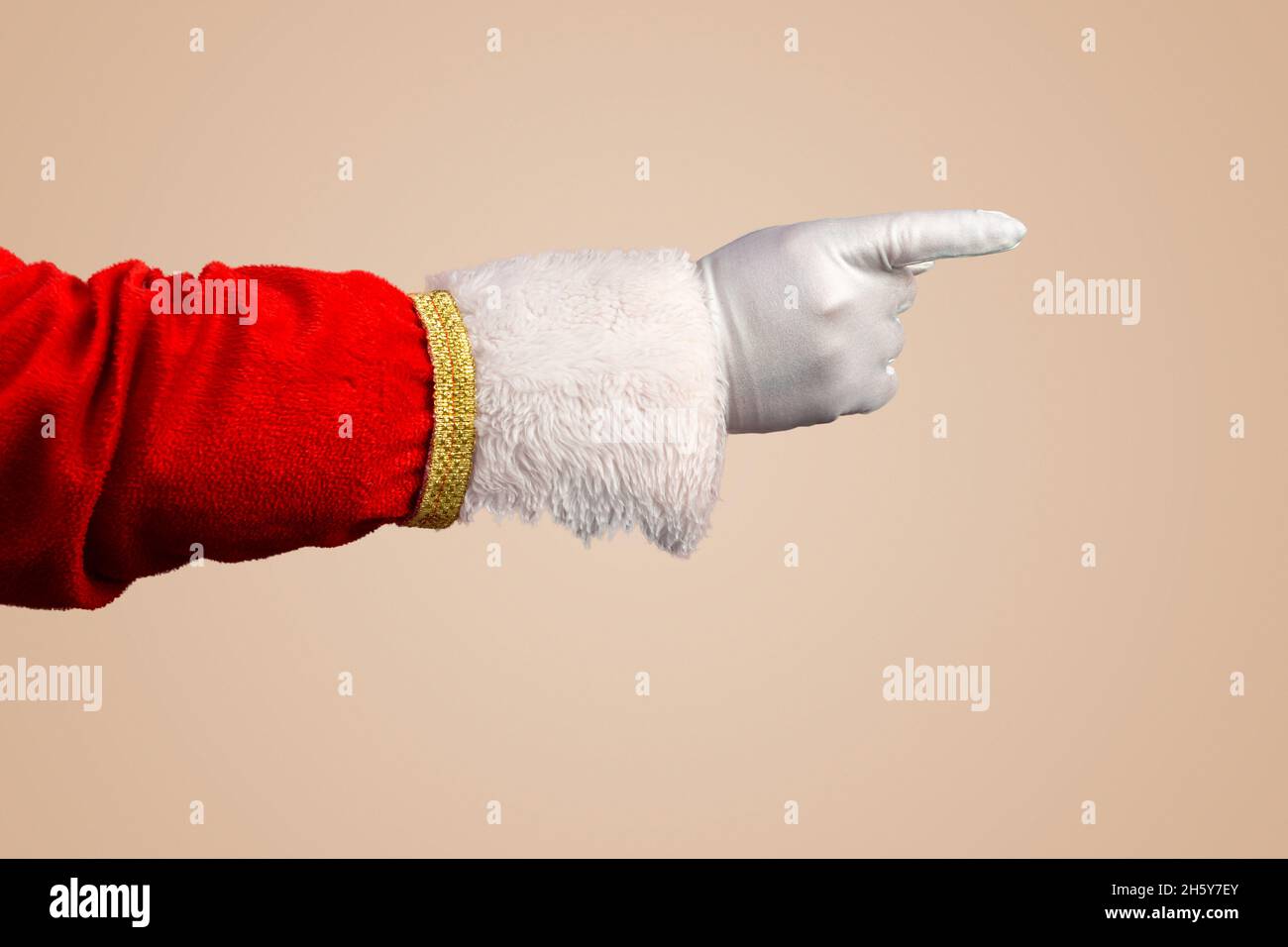 Foto di Babbo Natale guanto la mano nel gesto di puntamento. Babbo Natale punta le dita su pastello beige. Mano e braccio solo in formato orizzontale. Foto Stock
