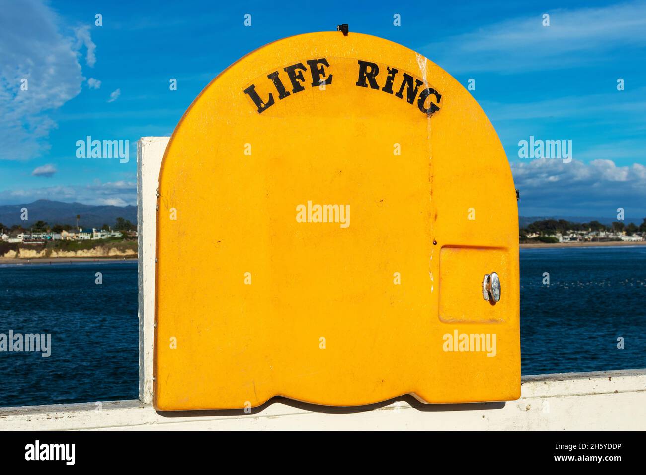 Armadio Life Ring con copertura gialla sulla ringhiera del molo. Sfondo sfocato e panoramico della costa dell'oceano. Foto Stock