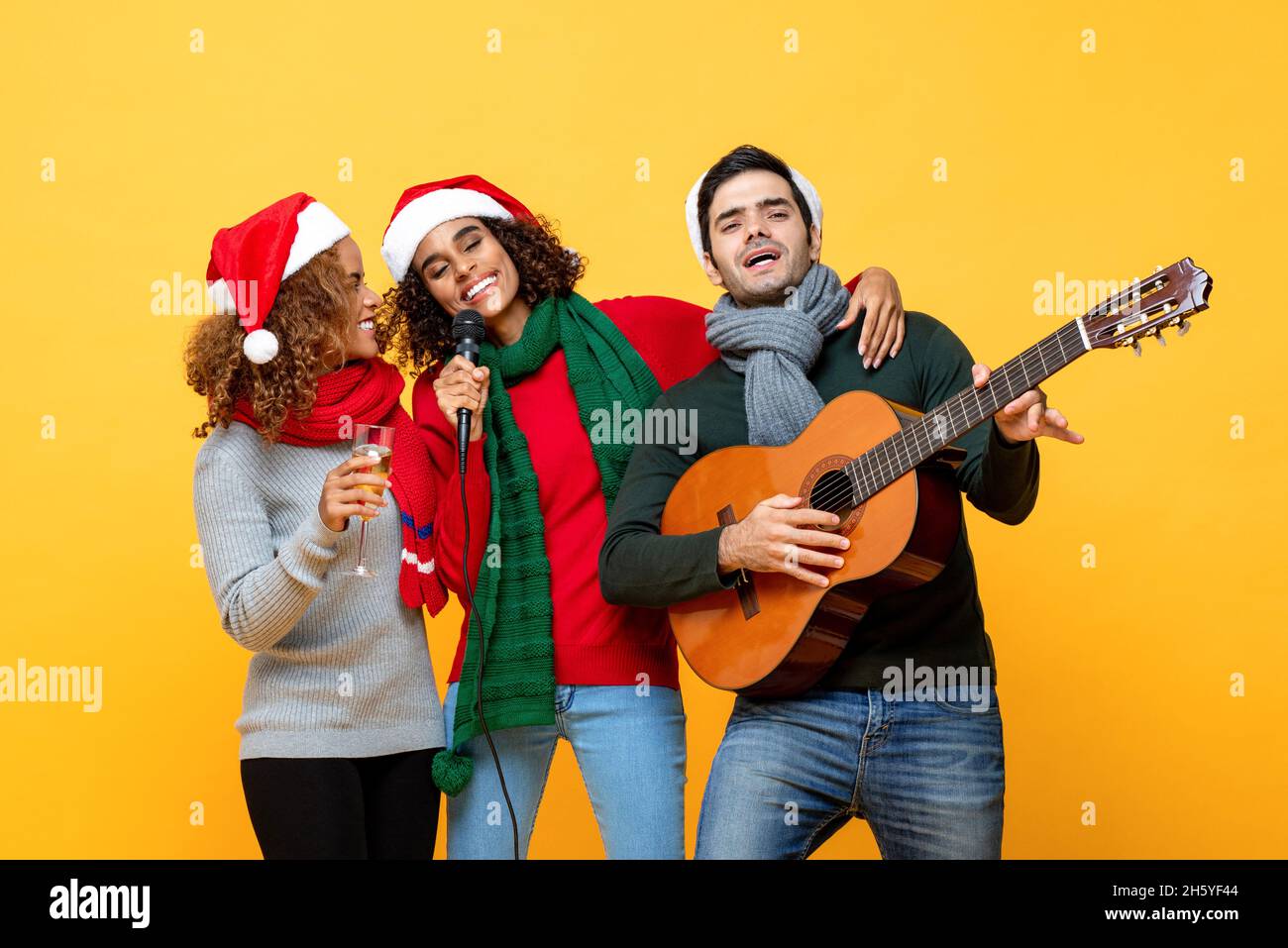 Gruppo multietnico di amici vicini che hanno partito cantando e celebrando il Natale in giallo studio isolato sfondo Foto Stock