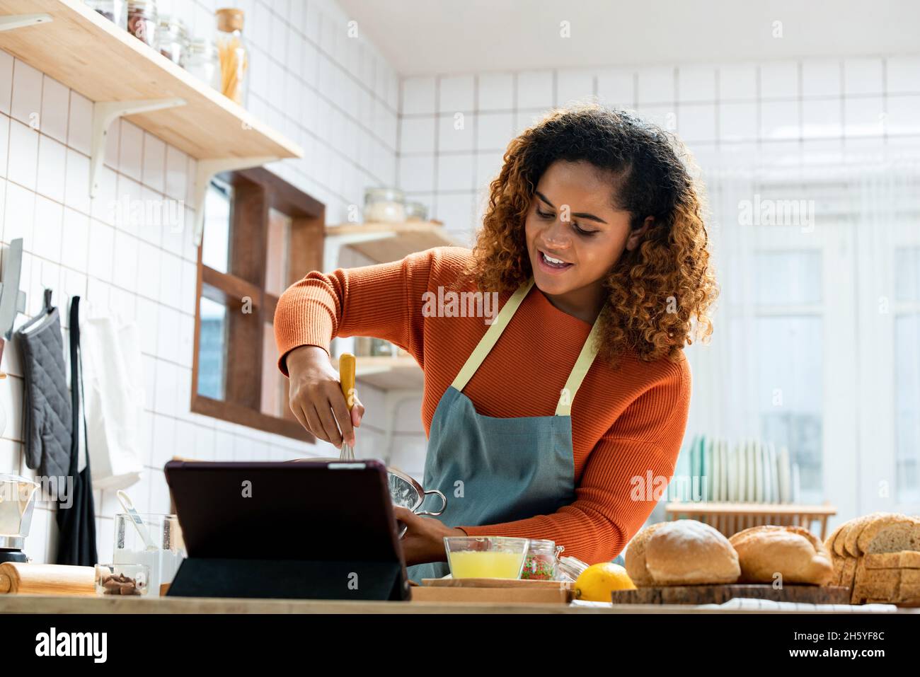 Giovane donna afroamericana in streaming video live insegnamento cucina panetteria online in cucina a casa Foto Stock