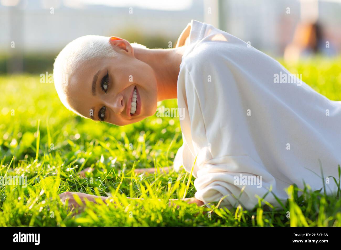 Ritratto di giovane 20s sorridente milleniale europeo capelli corti donna facendo asse bar sul verde prato parco estivo. Bella ragazza bionda felice all'aperto. Foto Stock