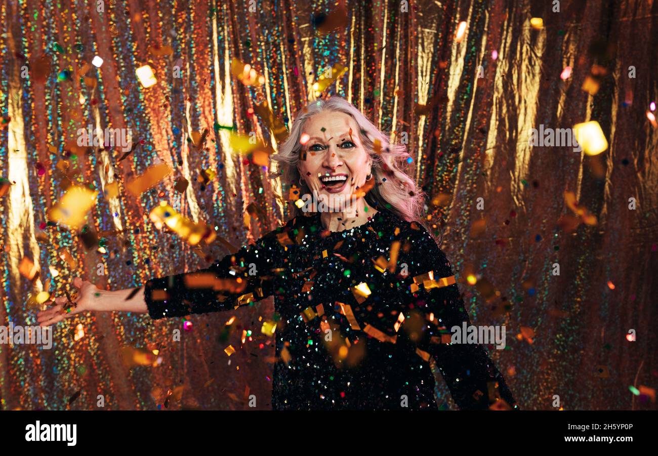 Donna anziana elegante in abito nero che lancia i confetti su uno sfondo dorato Foto Stock