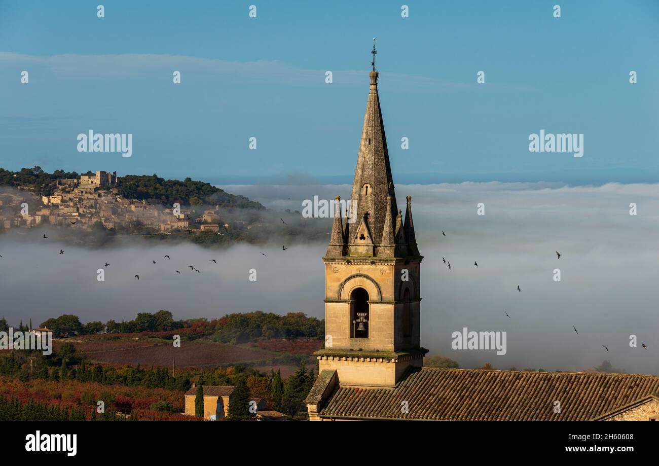 Vista della torre della chiesa a Bonnieux villaggio hiitop in provenza Francia con Lacoste sullo sfondo misteriosa mattinata d'autunno visto dal monte luberon Foto Stock