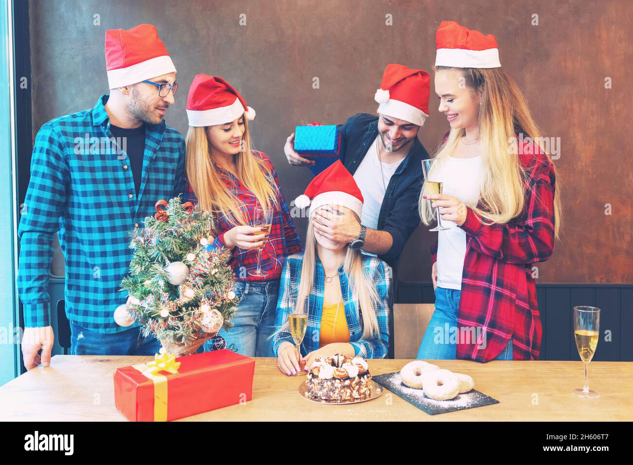 Gruppo di amici con cappelli Babbo Natale festeggiando regali e bevendo champagne a festa Foto Stock