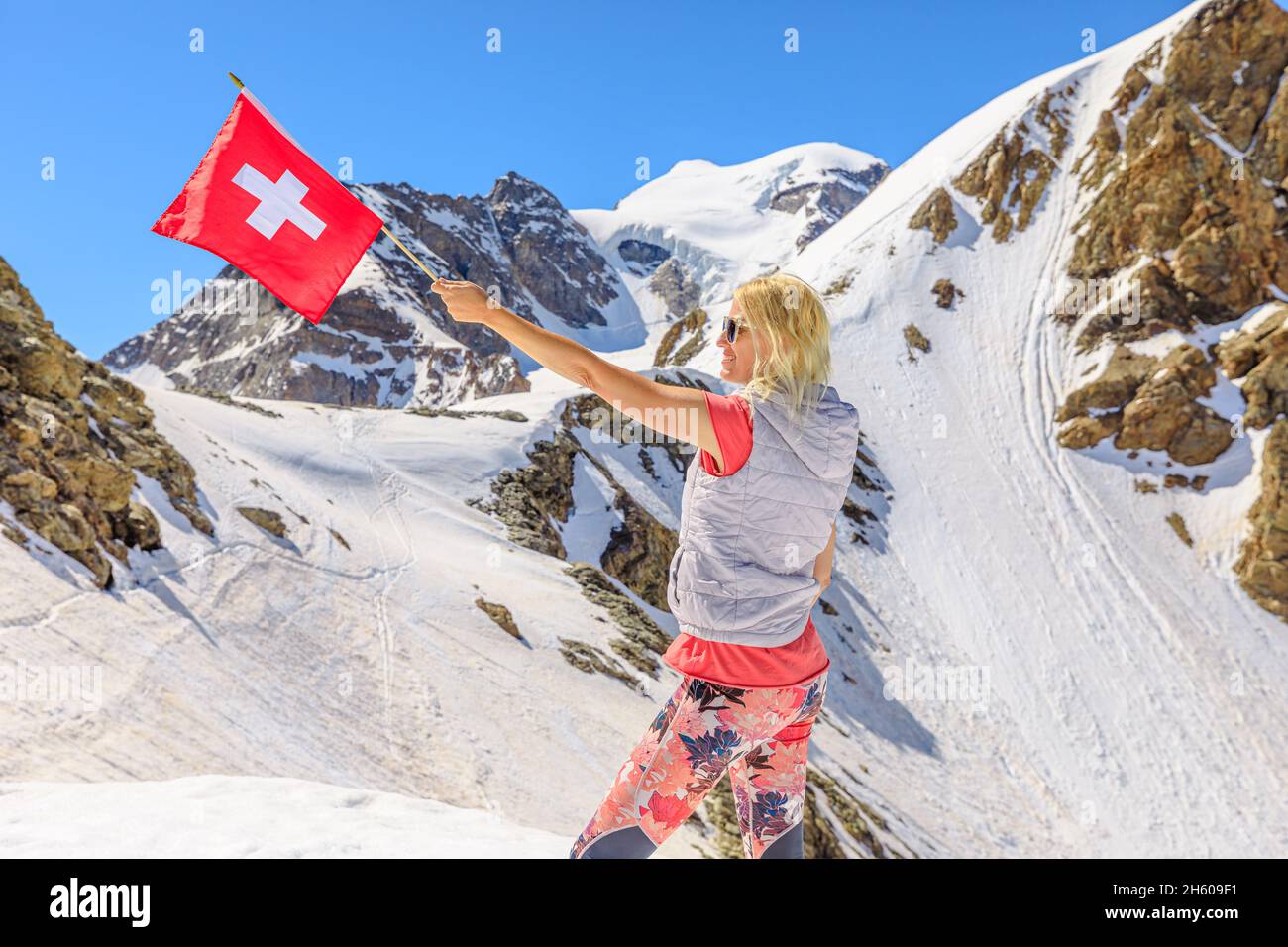 Primo piano della bandiera svizzera e di una ragazza turistica nella neve di Diavolezza in Svizzera. Vista dello skyline di Piz Bernina con il ghiacciaio Morteratsch a Graubunden Foto Stock