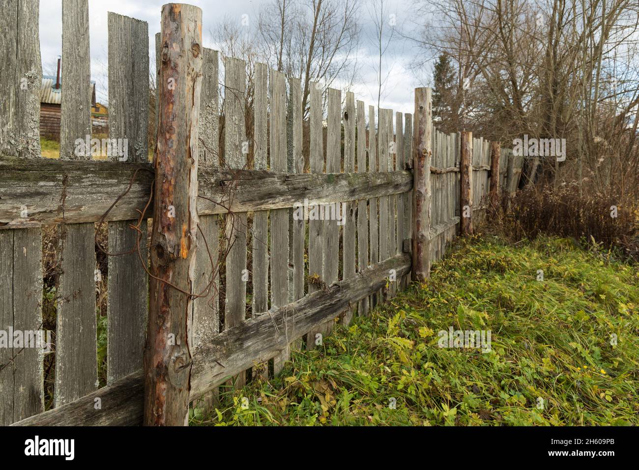 Palisata in legno che separa il terreno con un campo e arbusti Foto Stock