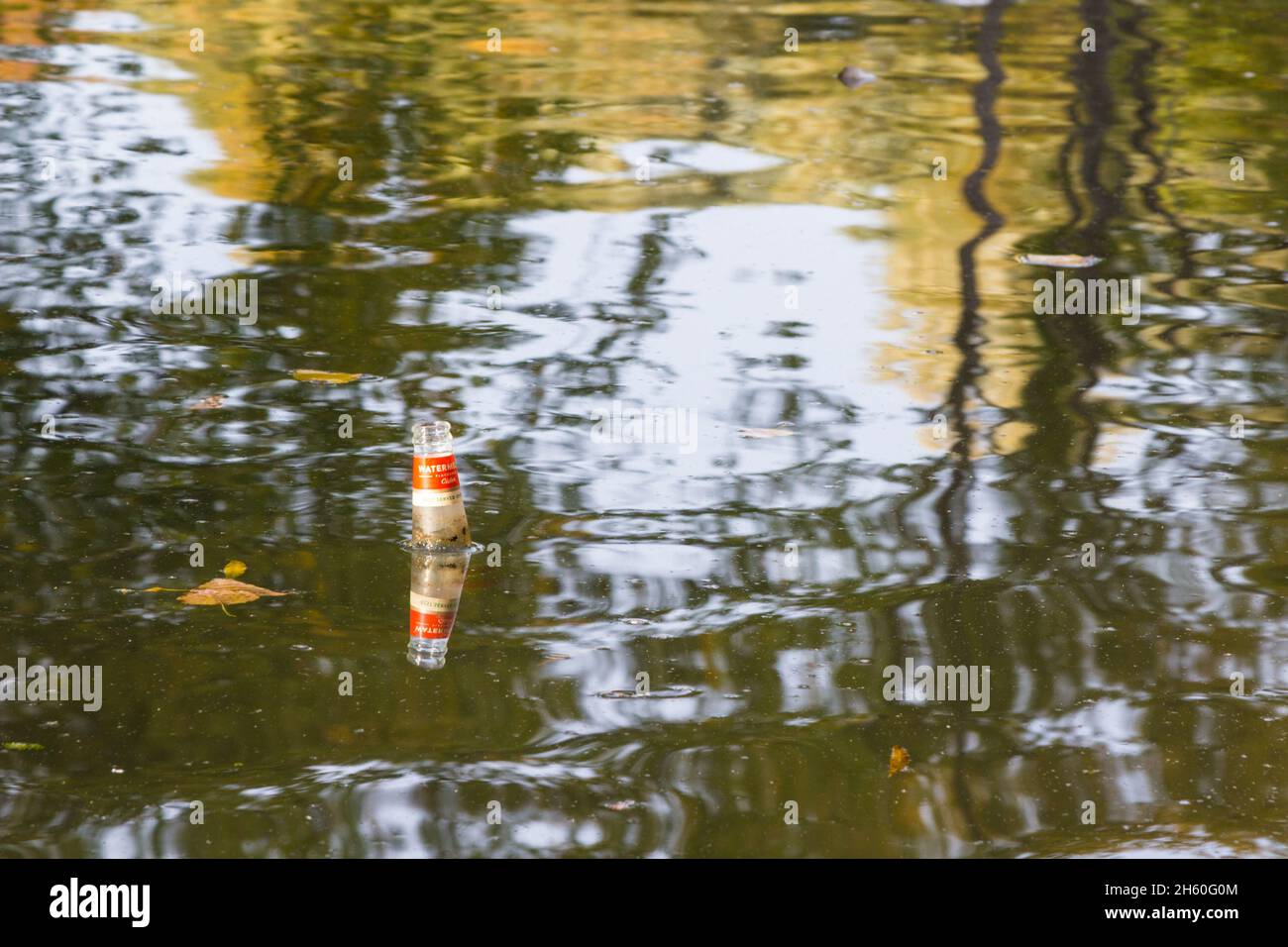 Una bottiglia vuota di sidro aromatizzata al melone Somersby gettata nell'acqua del lago galleggiante sulla superficie Foto Stock