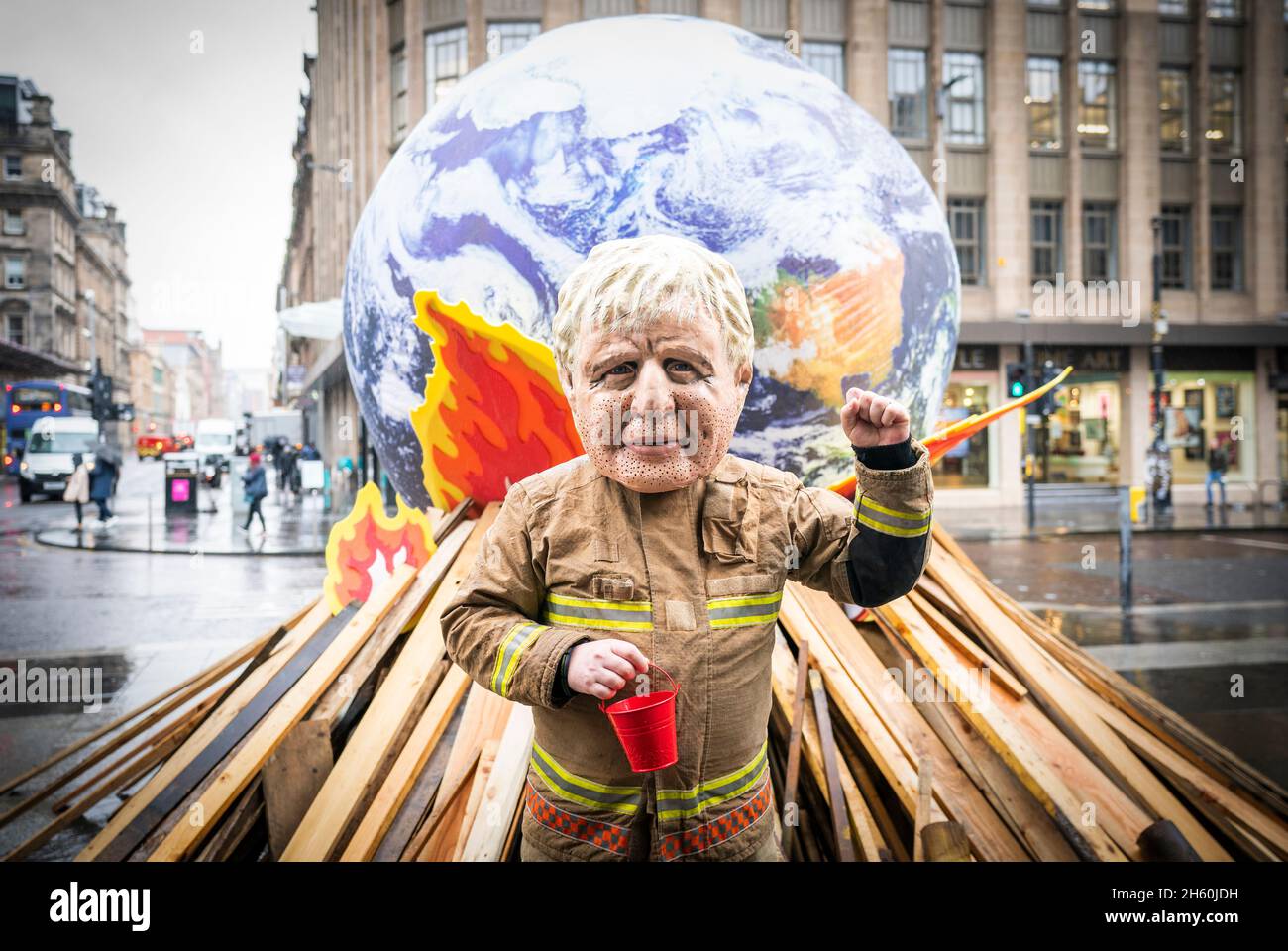 L'attivista che indossa i "grandi capi" di Boris Johnson partecipa all'esibizione di protesta dei leader mondiali di Oxfam contro l'inefficace incendio di fronte a un globo di 10 metri con un falò simulato, durante l'ultimo giorno ufficiale del vertice Cop26 a Glasgow. Data foto: Venerdì 12 novembre 2021. Foto Stock