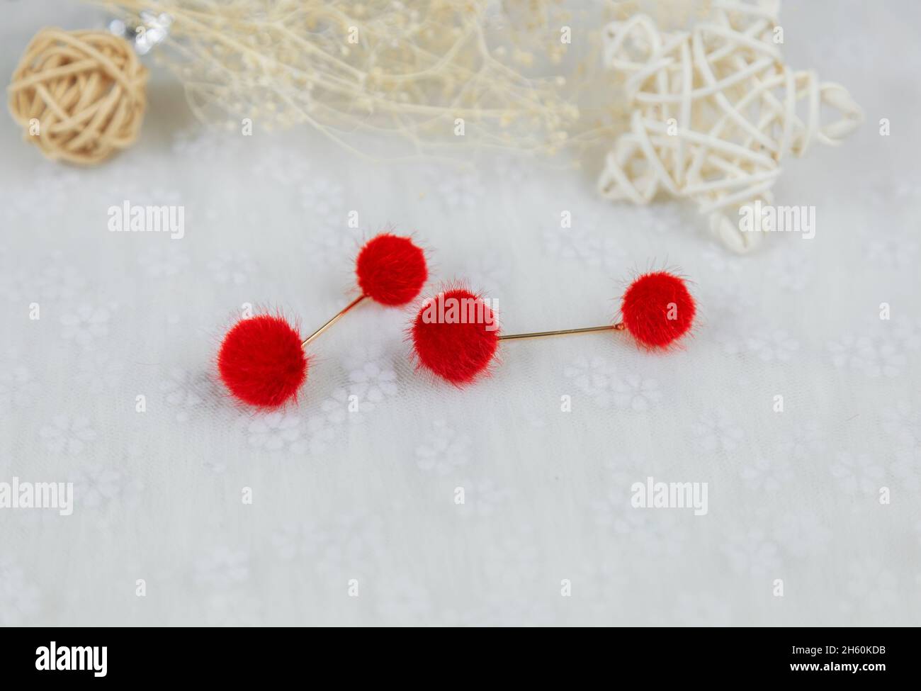 Orecchini di pompon rosso a forma di due soffici palle.Orecchini sono accanto a prodotti di rattan, esemplari di fiori e altri ornamenti Foto Stock