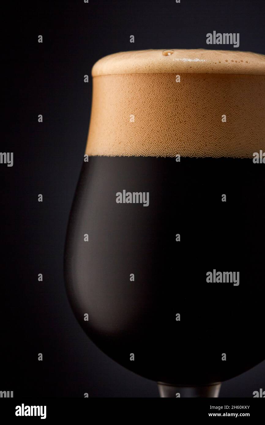 Primo piano di un bicchiere di birra scura su sfondo nero. Foto Stock