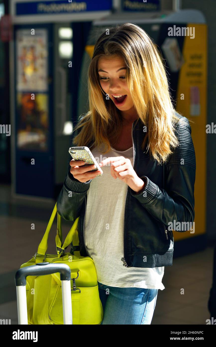 GIOVANE DONNA DI 18 ANNI IN UNA STAZIONE FERROVIARIA DI CONSULENZA IL SUO CELLULARE Foto Stock