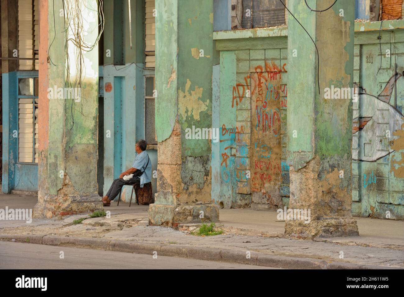Scena stradale nel centro di l'Avana. Architettura coloniale sbriciolante con uomo seduto, la Habana (l'Avana), Habana, Cuba Foto Stock