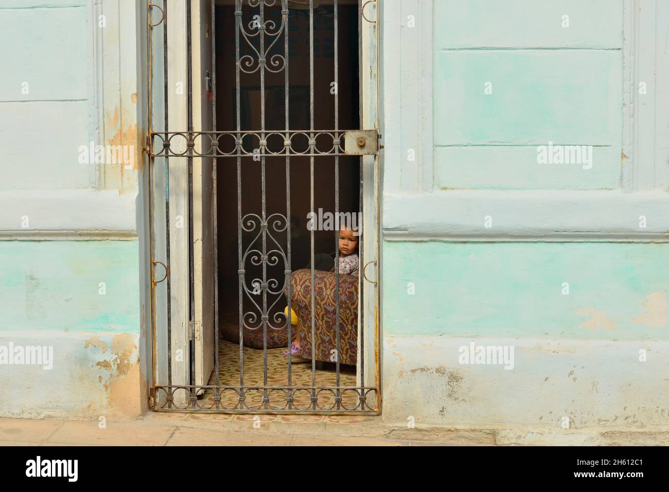Scena stradale nel centro di l'Avana. Bambino piccolo che guarda fuori attraverso una porta con cancello, la Habana (l'Avana), Habana, Cuba Foto Stock