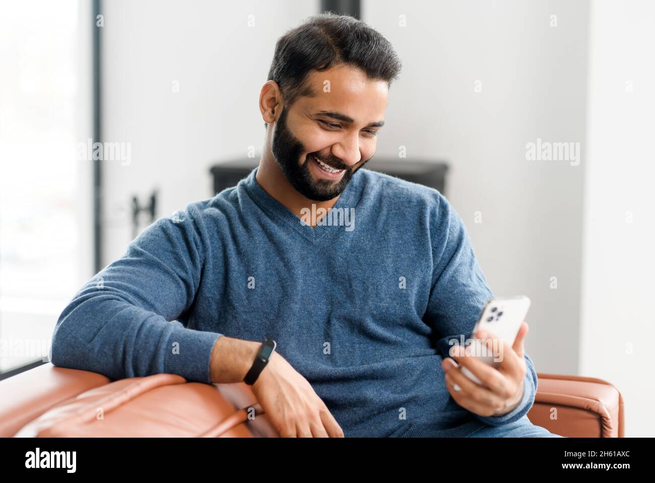 Bel ragazzo indiano che usa uno smartphone per videochiamare, uomo  sorridente in abbigliamento casual che parla con la webcam, godendo di  incontri virtuali con un amico o una ragazza seduta sul divano
