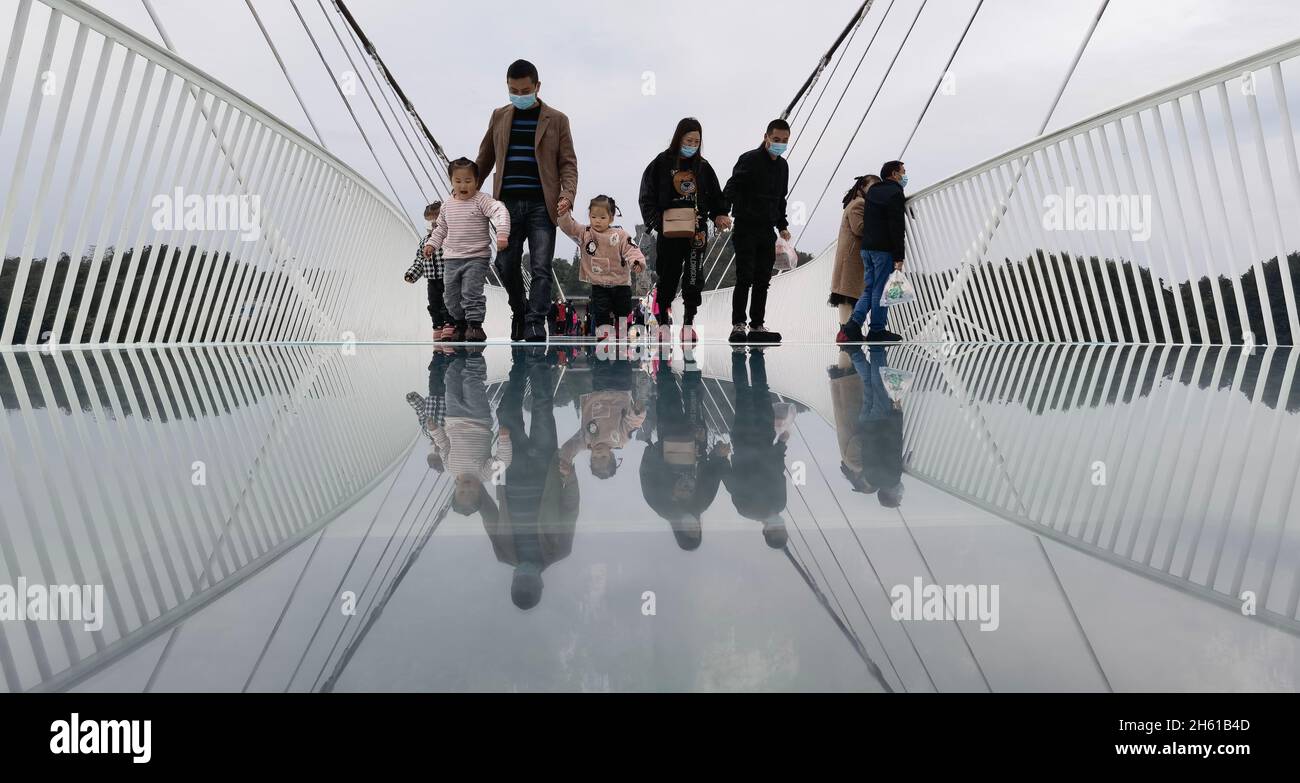 Zhangjiajie, la provincia cinese Hunan. 12 novembre 2021. I turisti camminano su un ponte dal fondo di vetro al Grand Canyon di Zhangjiajie, nella provincia di Hunan della Cina centrale, 12 novembre 2021. Il ponte lungo 430 metri, largo sei metri, che collega due ripide scogliere a 300 metri dal suolo, è lastricato con 99 lastre di vetro trasparente a tre strati. Credit: Zhao Zhongzhi/Xinhua/Alamy Live News Foto Stock