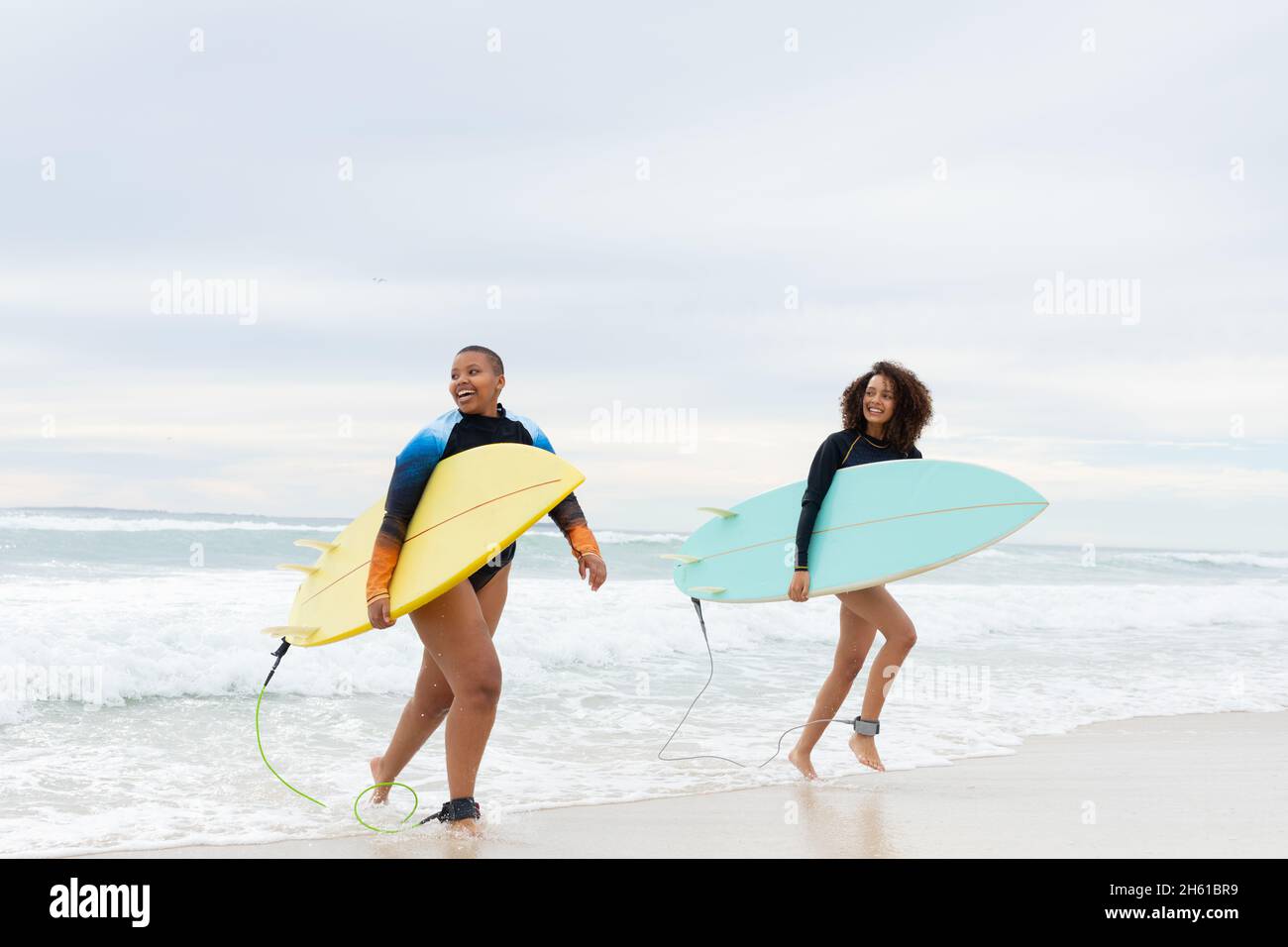 Sorridenti amici femminili multirazziali con tavole da surf che corrono a riva del mare contro il cielo durante il fine settimana Foto Stock