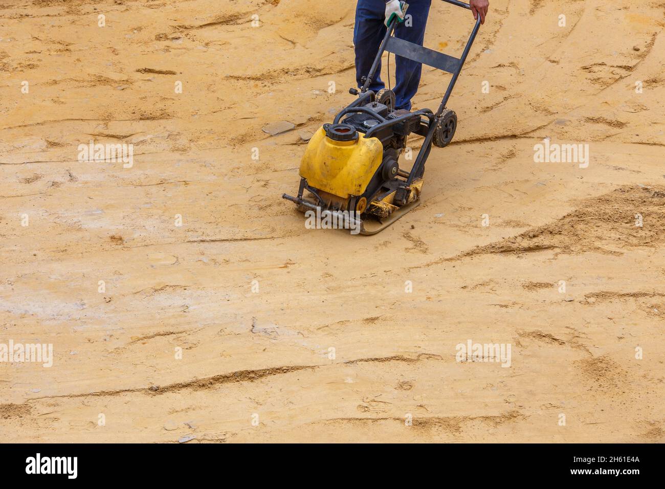 Operatore in uso compattatore a piastre vibranti per la compattazione della sabbia durante la costruzione del percorso. Foto Stock