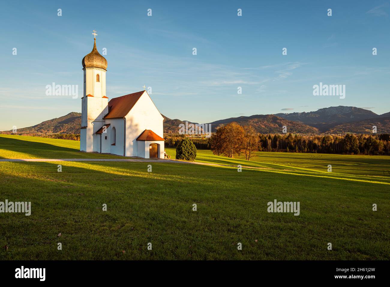 La Cappella Barocca di San Giovanni sopra la Valle di Loisach e le Prealpi autunnali bavaresi con il Monte Benediktenwand al sole serale, in Germania Foto Stock