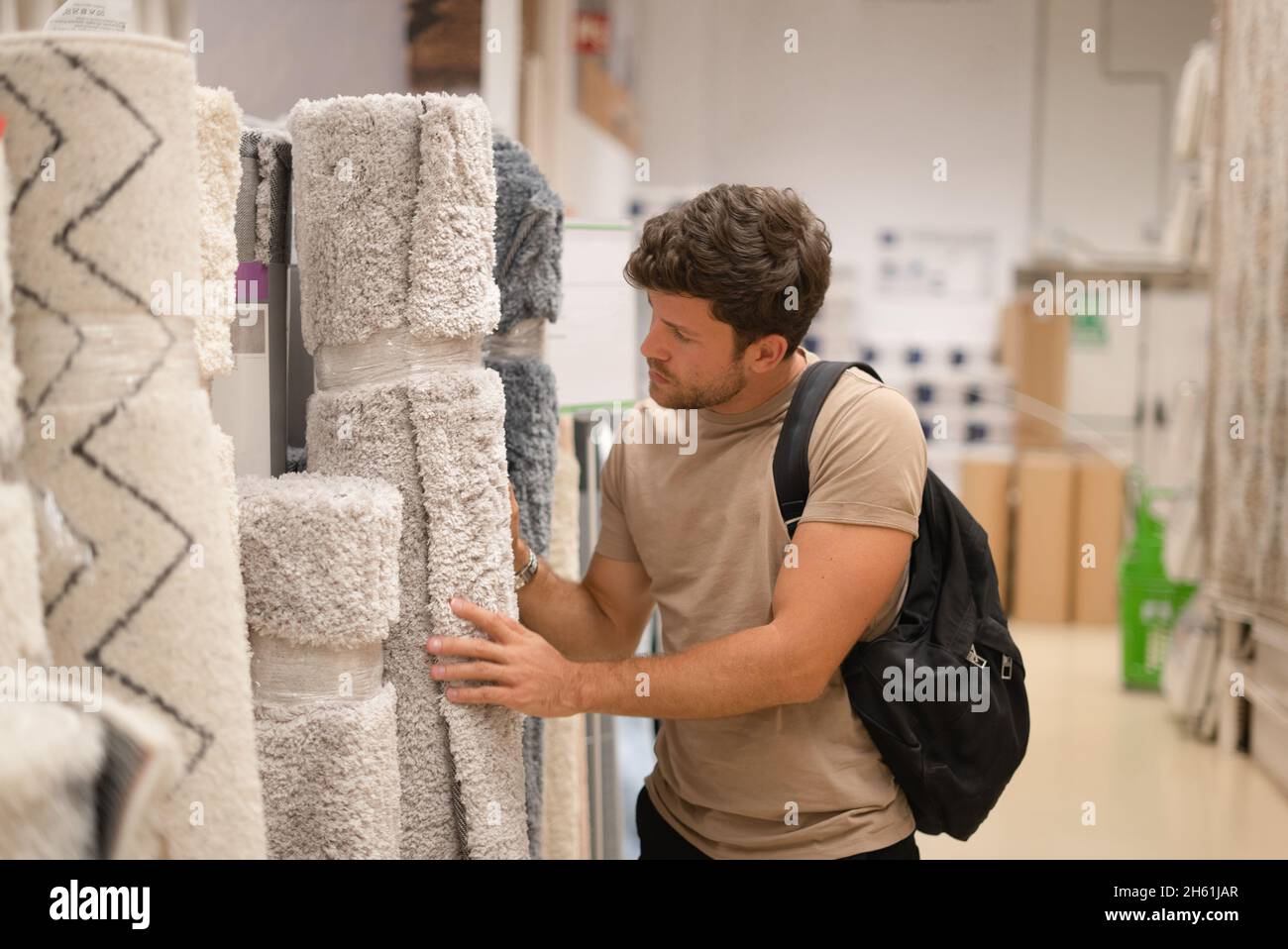 Ragazzo giovane concentrato con zaino guardando morbido tappeto grigio in rotolo, mentre shopping nel reparto di arredamento Foto Stock