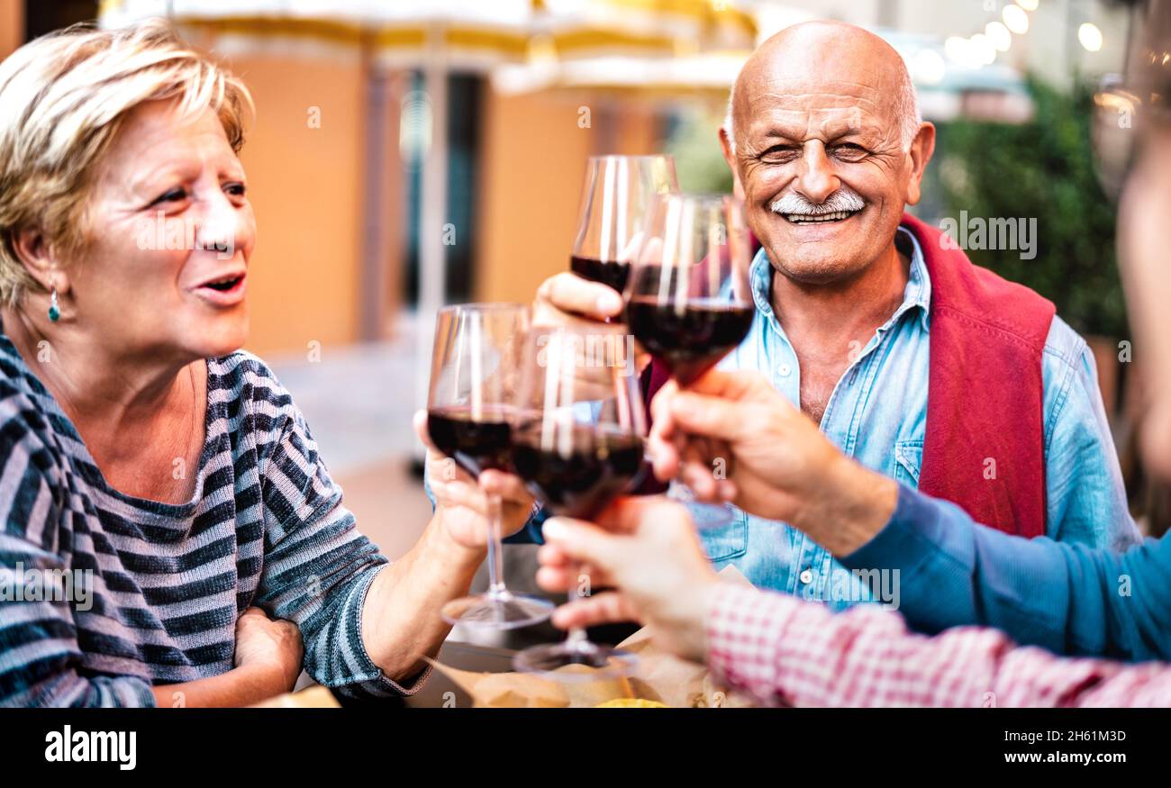 Coppia anziana felice divertirsi bevendo vino rosso con gli amici a cena partito - pensionati che mangiano insieme al ristorante balcone Foto Stock